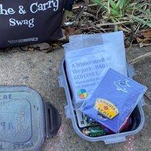 Yellow Canadian Cacher pin in a small cache with assorted trade items and a cache description