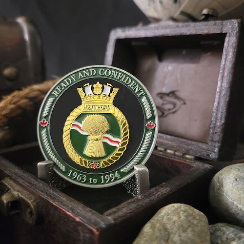 Front view of HMCS Saskatchewan challenge coin in a display case. The coin displays the Saskatchewan Ship crest surrounded by a border with the phrase 