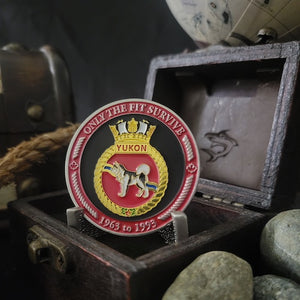 Front view of our HMCS Yukon challenge coin in a display case.The coin displays the Yukon Ship crest surrounded by a border with the phrase "Only the Fit Survive" at the top, and "1963 to 1993" at the bottom