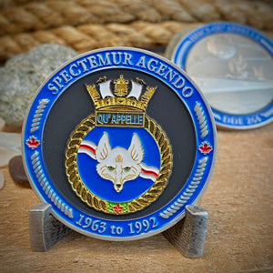 Front view of Qu'Appelle challenge coin in a display stand. The coin displays the Qu'Appelle Ship crest surrounded by a border with the phrase "Spectemur Agendo" at the top, and "1963 to 1992" at the bottom