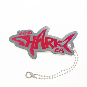 Shark shaped Landsharkz trackable tag that says Landsharkz in red, attached to a ball chain