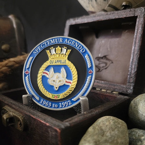 Front view of Qu'Appelle challenge coin in a display case. The coin displays the Qu'Appelle Ship crest surrounded by a border with the phrase 