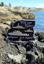 Three ships and one submarine in matte nickel on the back of the Royal Canadian Navy coin on rocks in front of the ocean