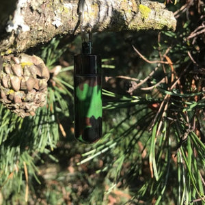 Camo micro geocache container hanging on a branch in a pine tree. the geocache container blends into the environment.