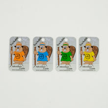 four trackable tags with beaver dude in 4 different shirt colours. Beaver dude is holding a wood hiking stick.