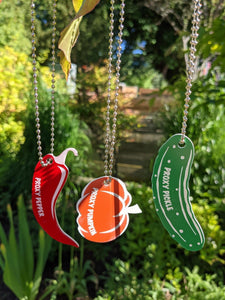 Three proxy tags hanging on ball chains, a red pepper, an orange pumpkin and a green pickle 